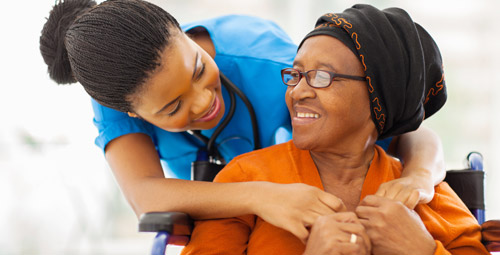 An older woman being hugged from behind by a healthcare professional
